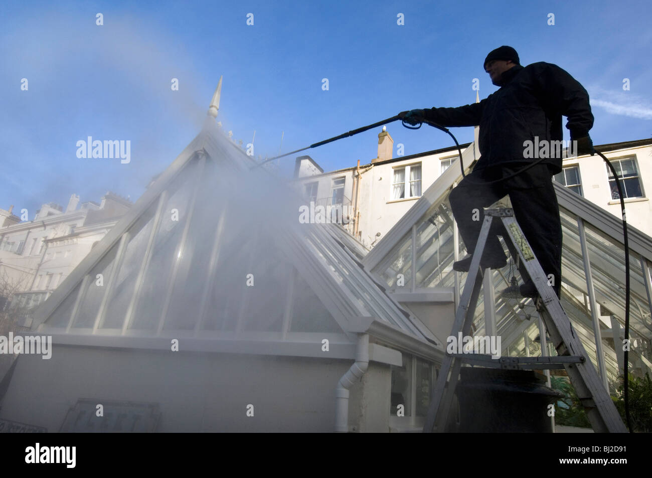 A man power-washing a greenhouse with a jet spray. Stock Photo