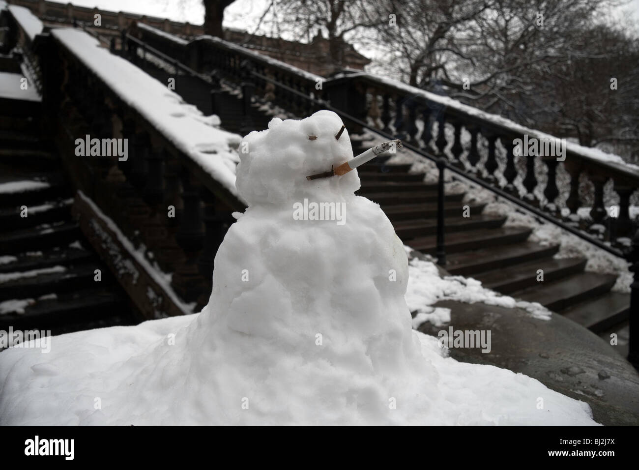 A mini snowman with a lit cigarette in its mouth atop a stone banister in Edinburgh's Princes Street Gardens Stock Photo