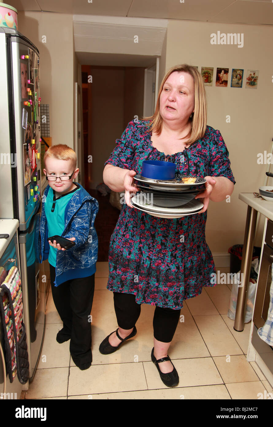 Woman carrying dirty plates in the kitchen with a child. Stock Photo