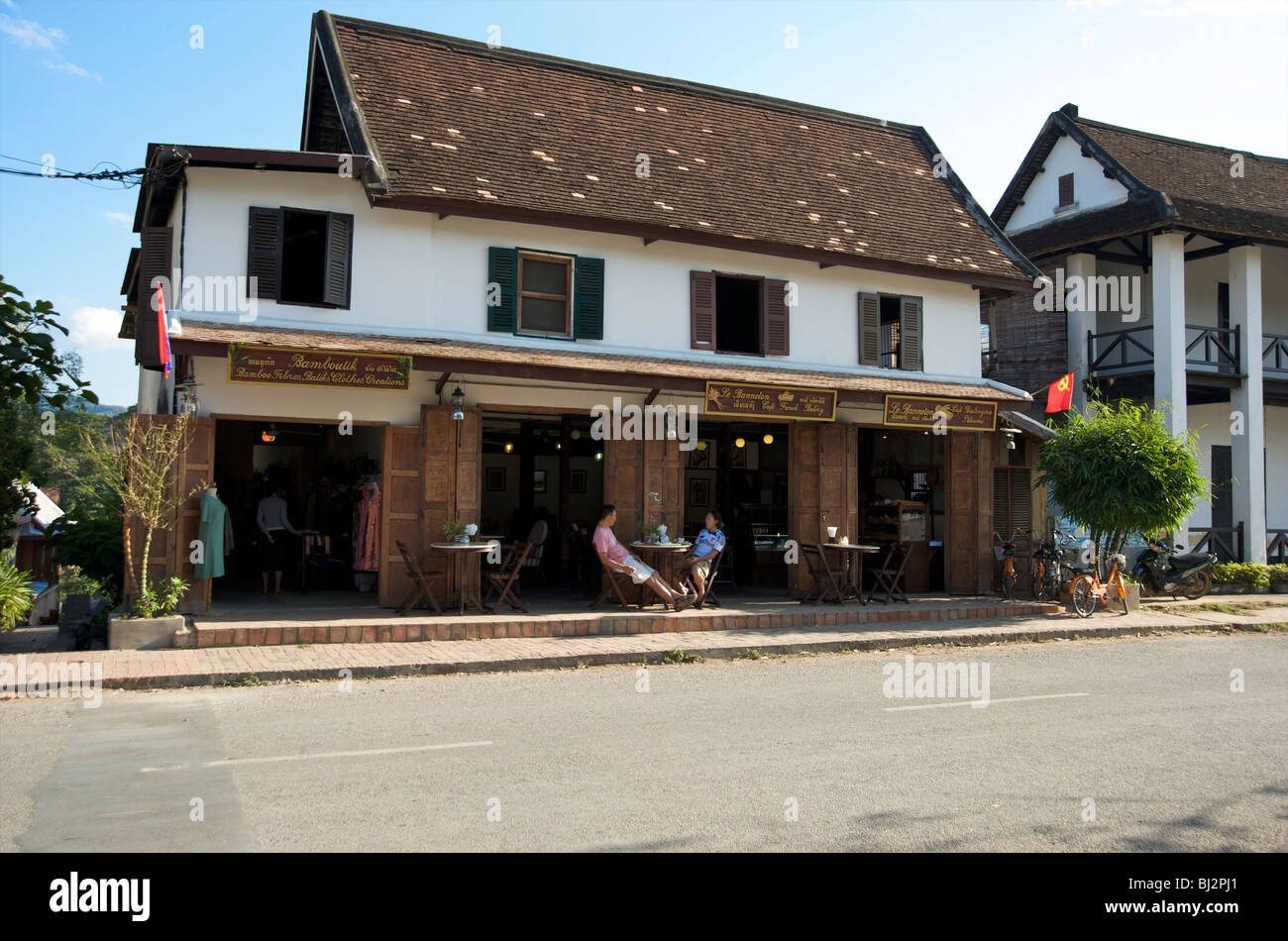 Tourists sit outside a French colonial villa converted into a hotel and bakery in Luang Prabang Laos Stock Photo