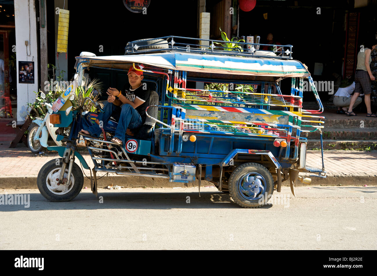 A Tuk Tuk driver rests on his taxi in Luang Prabang Laos Stock Photo