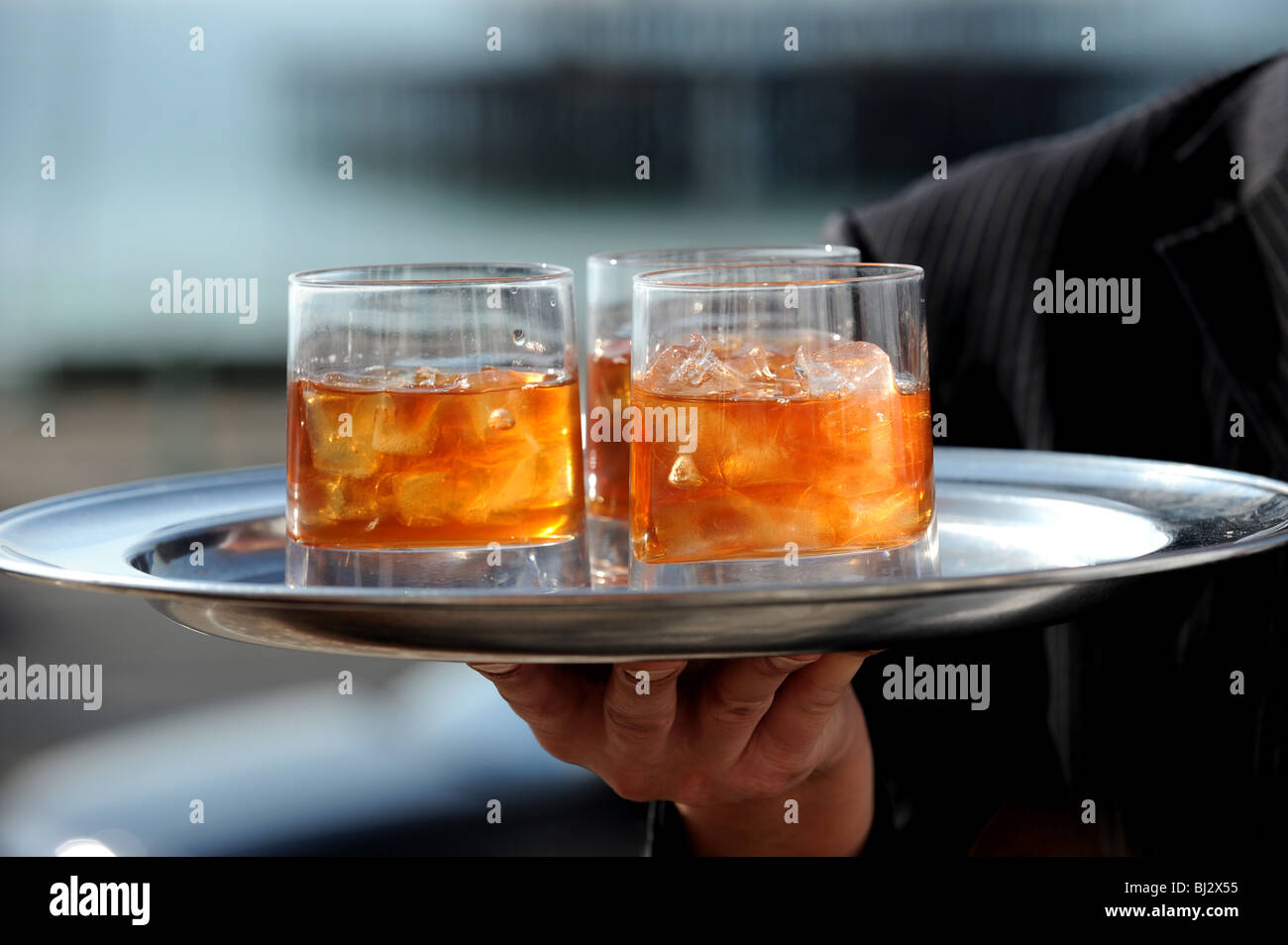 Tumbler glasses of whisky with lumps of ice cubes on a tray held by hand in front of West Pier Brighton seafront Stock Photo