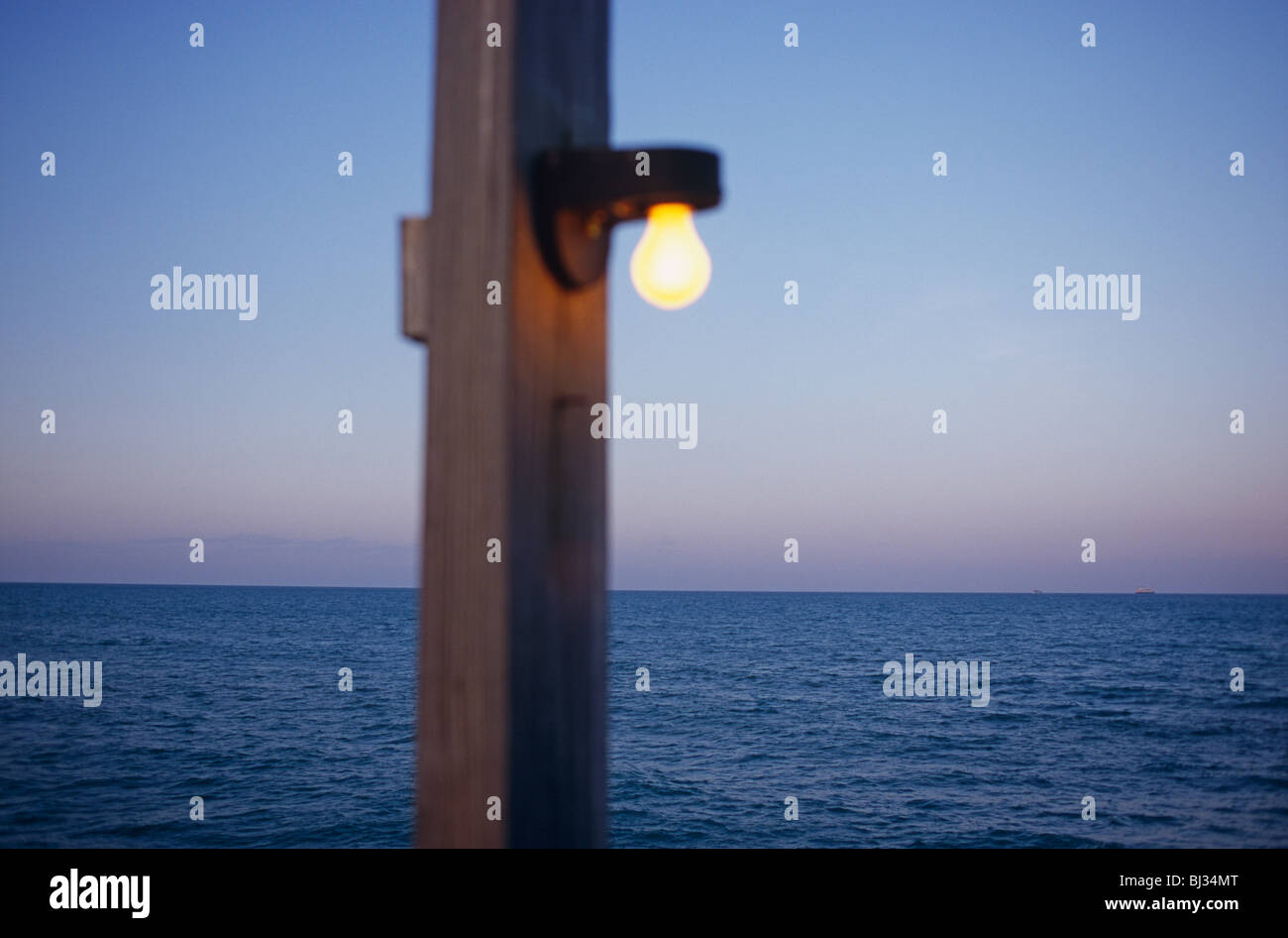 Out of focus post with a light bulb attached, shines in the bright daylight with the Atlantic Ocean beyond. Stock Photo