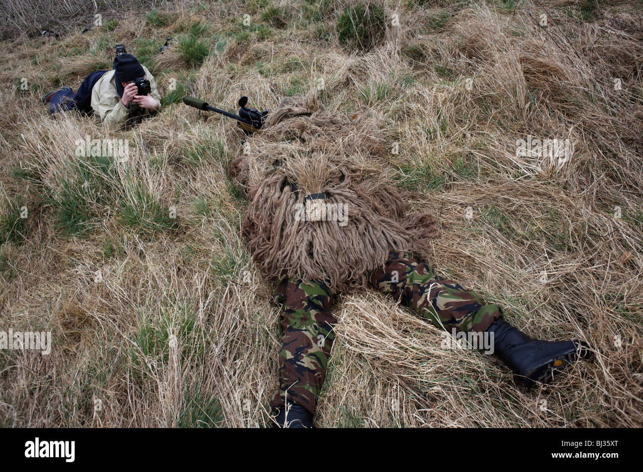 Watched by media, a camouflaged British infantry soldier is seen looking down the telescopic sight of a L115A3 sniper rifle. Stock Photo