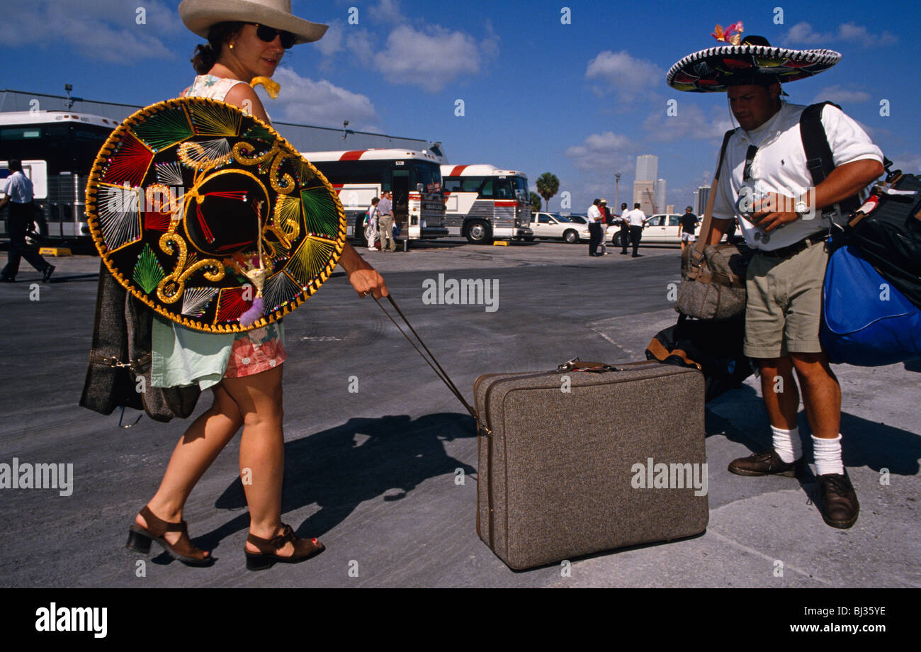 Wearing sombreros, two tourists carry and pull their baggage along to a waiting coaches after a cruise to Mexico. Stock Photo