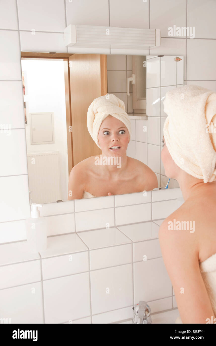 Young woman with a towel wrapped around her head in front of a mirror Stock Photo