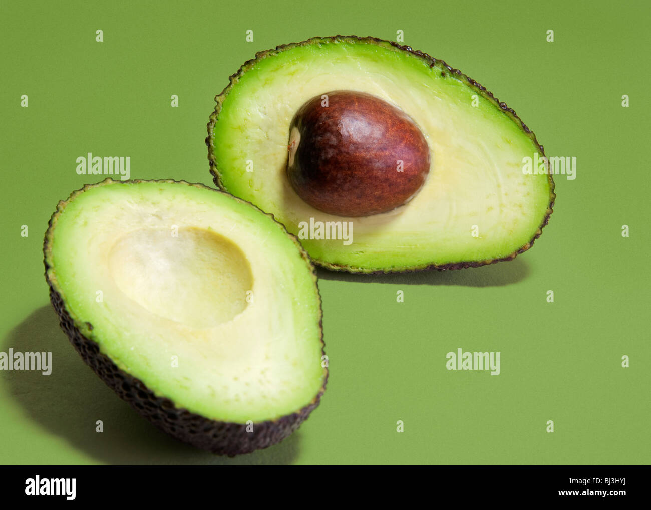 Hass variety avocado pear sliced into two halves against a green background. Stock Photo