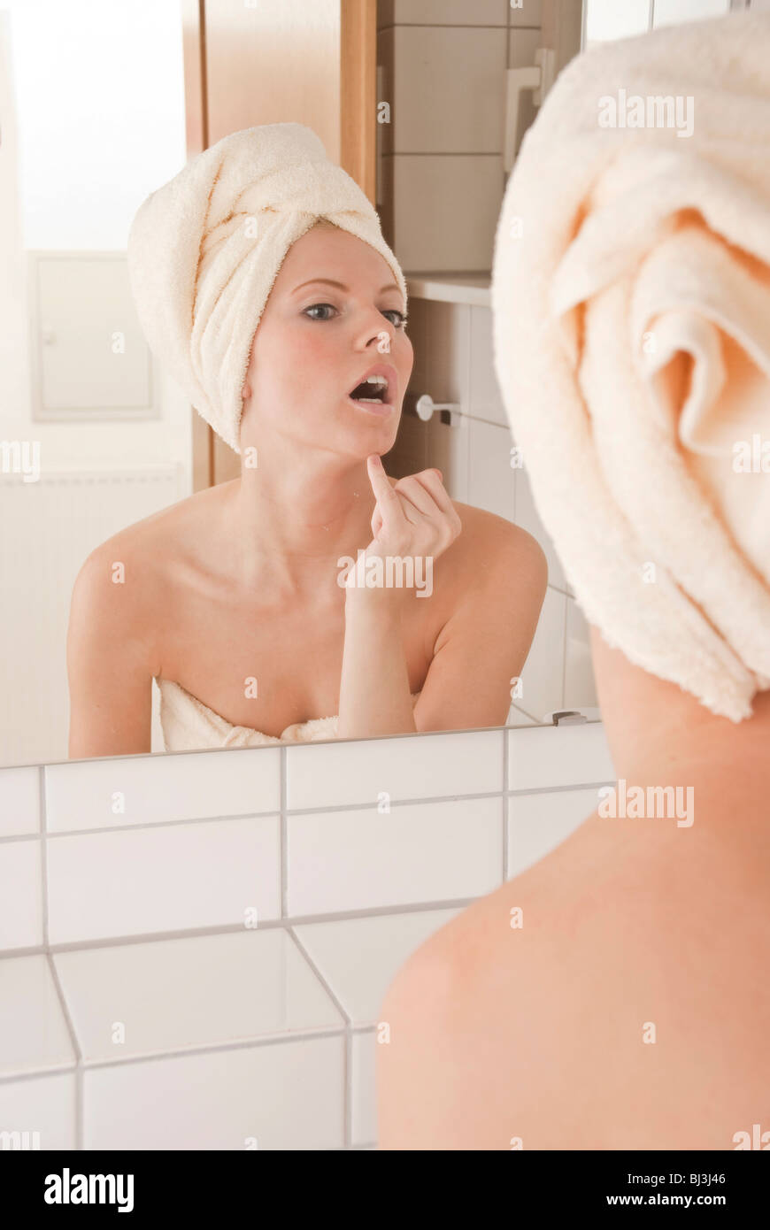 Young woman with a towel wrapped around her head in front of a mirror Stock Photo
