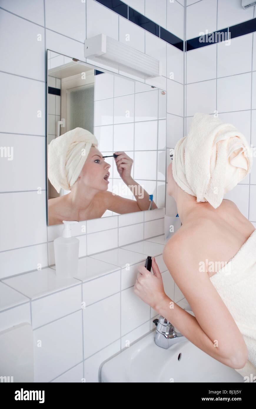 Women putting on mascara in front of the mirror in the bathroom Stock Photo