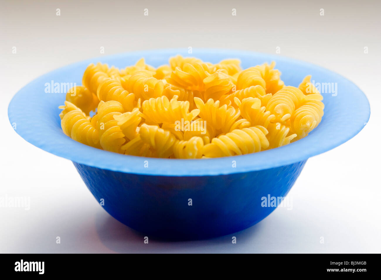 Organic dry pasta twirls in blue glass dish Stock Photo