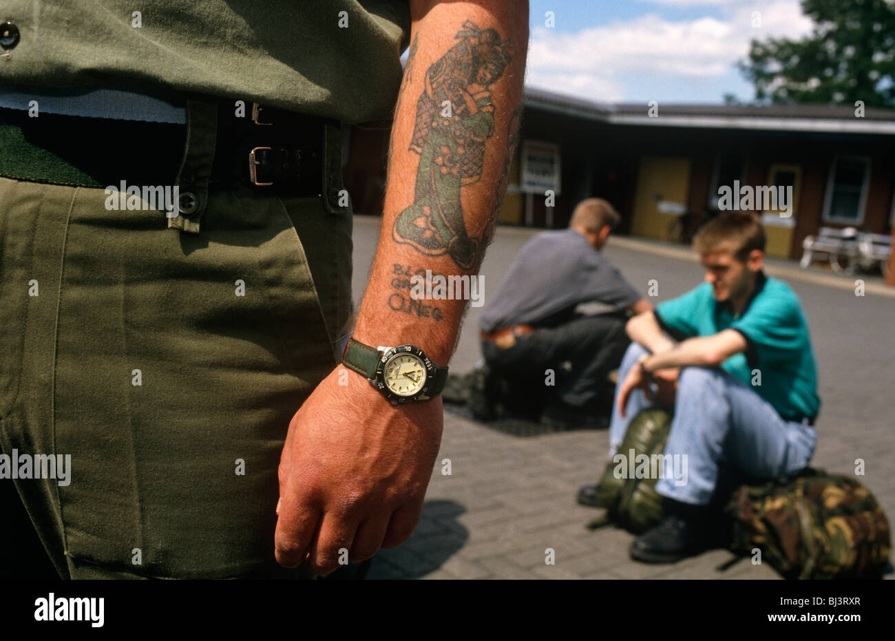 Strong tattooed forearm of a British army soldier and two part-time territorial army conscripts sitting ruck sacks. Stock Photo