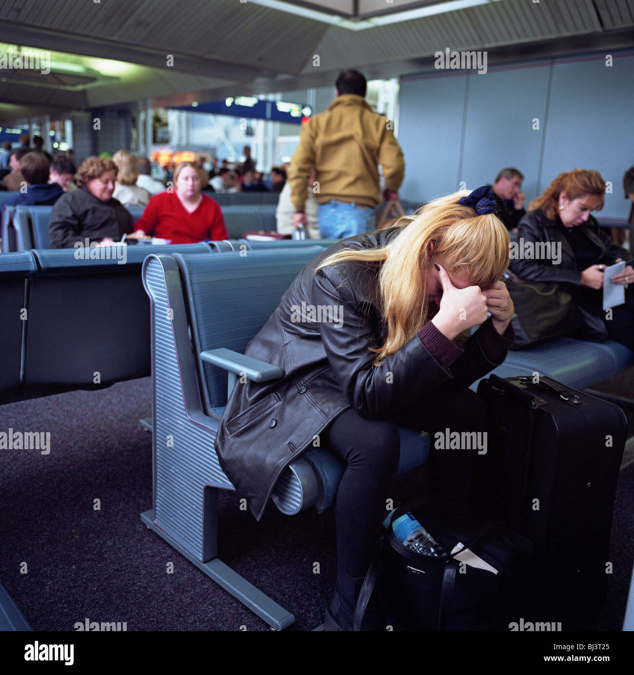 A female passenger leans forward with head in hands amid the busy terminal at Chicago O'Hare Airport. Stock Photo