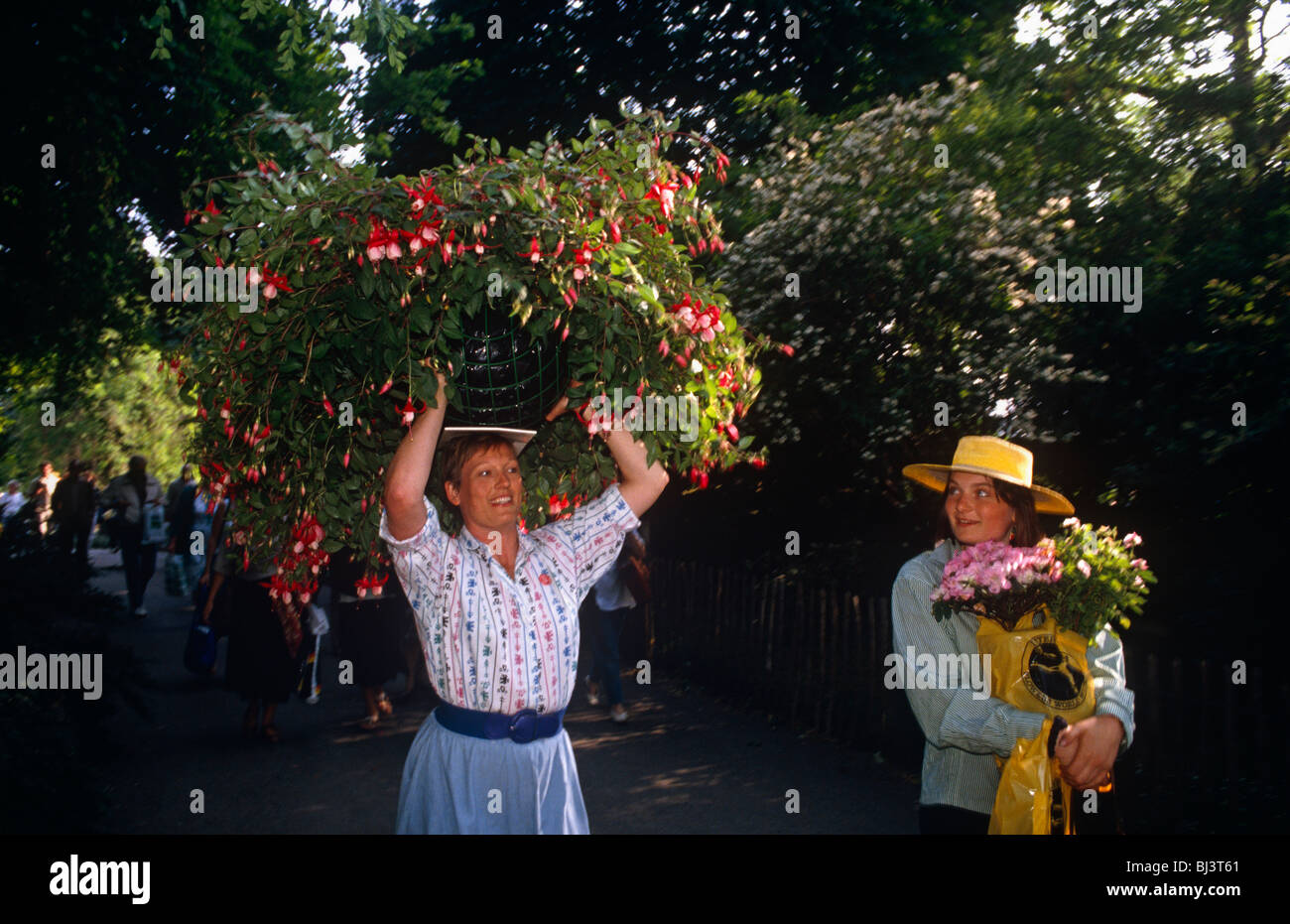 With a huge basket of Fuchsias on her head, a lady walks along a London street after the Chelsea Flower Show. Stock Photo