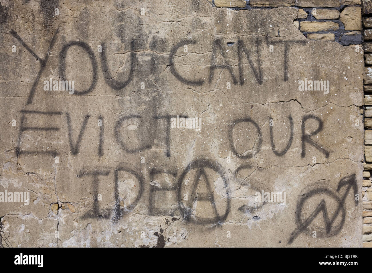 Anarchic graffiti sprayed on a rendered brick wall proclaims that a higher authority ‘Can’t evict our ideas’. Stock Photo