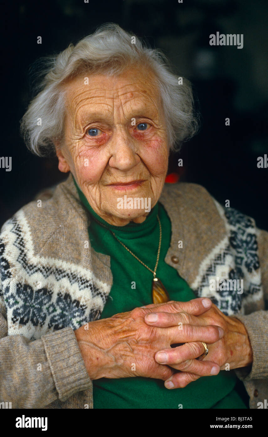A ninety year-old sits with fingers crossed looking to viewer with a mild look of mild bemusement and sadness. Stock Photo