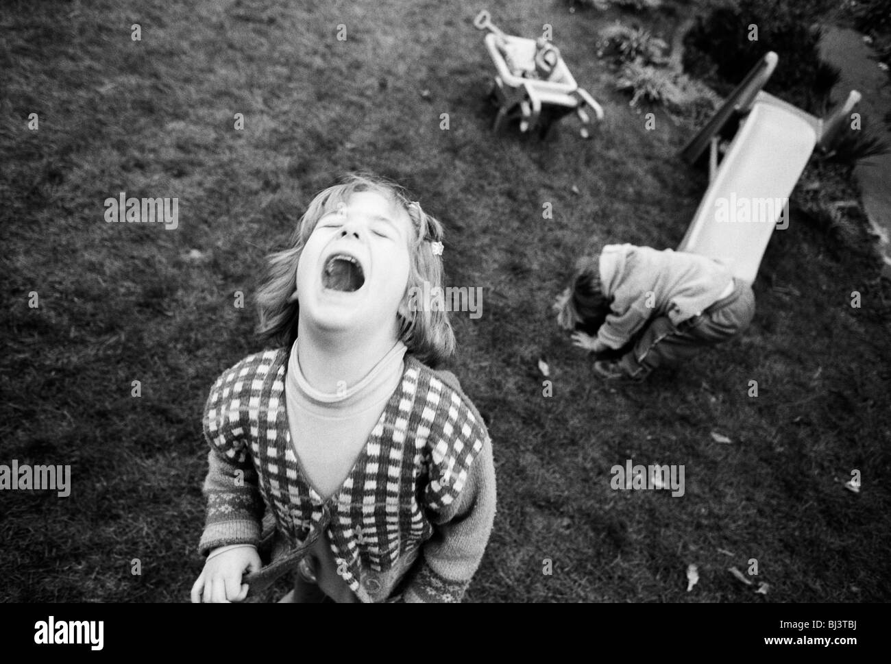 A four year-old girl throws a tantrum while playing with her young two-year-old brother in the back garden of their home. Stock Photo