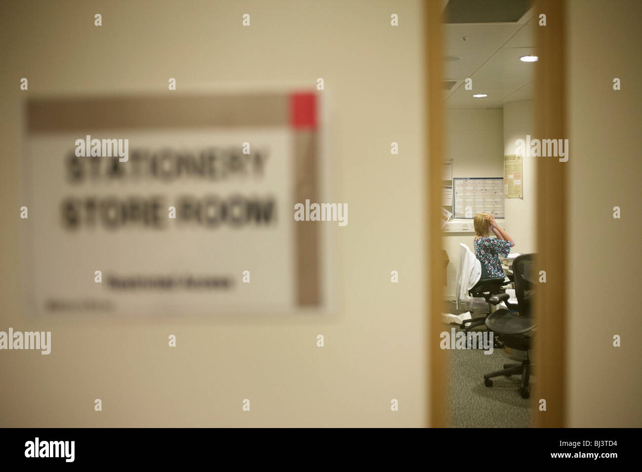 Peering through a narrow window into an office, we see a stretching female company employee in their London headquarters. Stock Photo