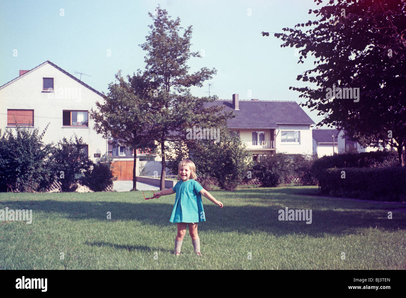 A young blonde girl of approximately 3 years-old stands on a lawn looking delighted in 1967. Stock Photo