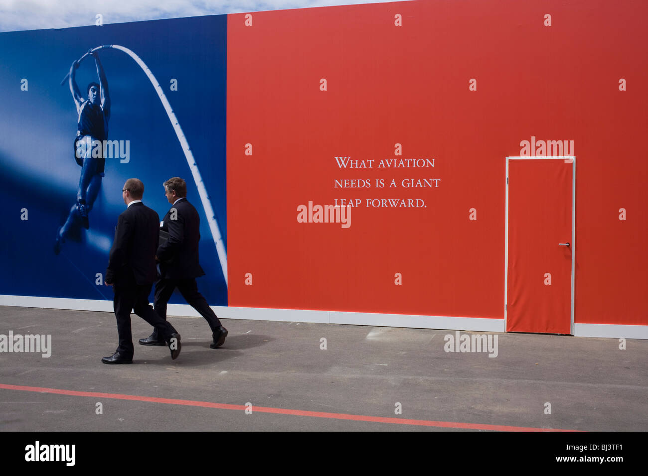 Two businessmen pass-by a slogan about the future of the aviation industry written on a red hoarding at Farnborough Air Show Stock Photo