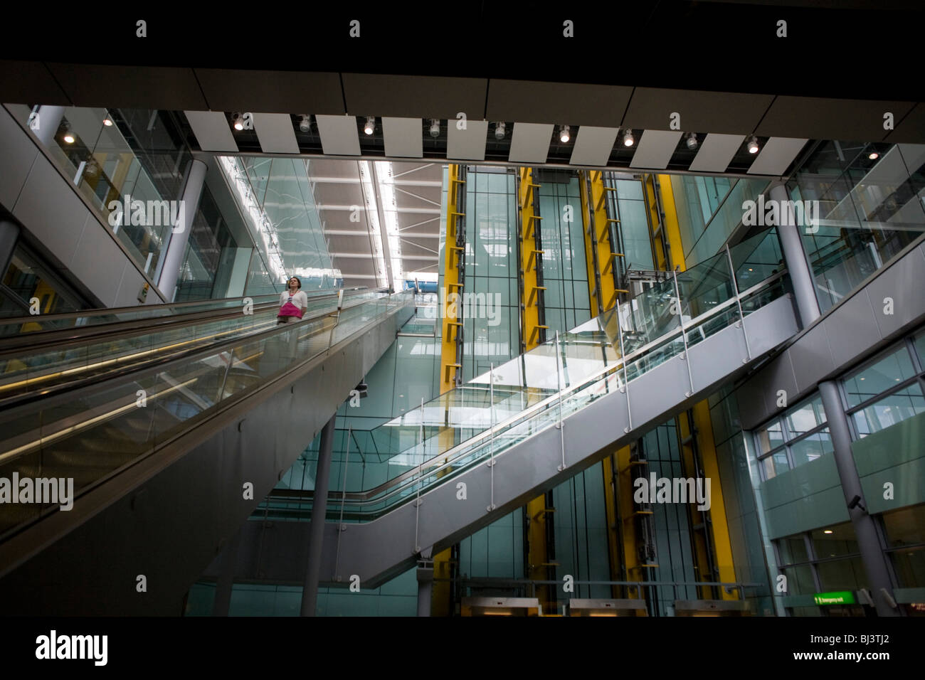 Lone departing female passenger descends one of the 105 escalators in Terminal 5 of London's Heathrow Airport. Stock Photo