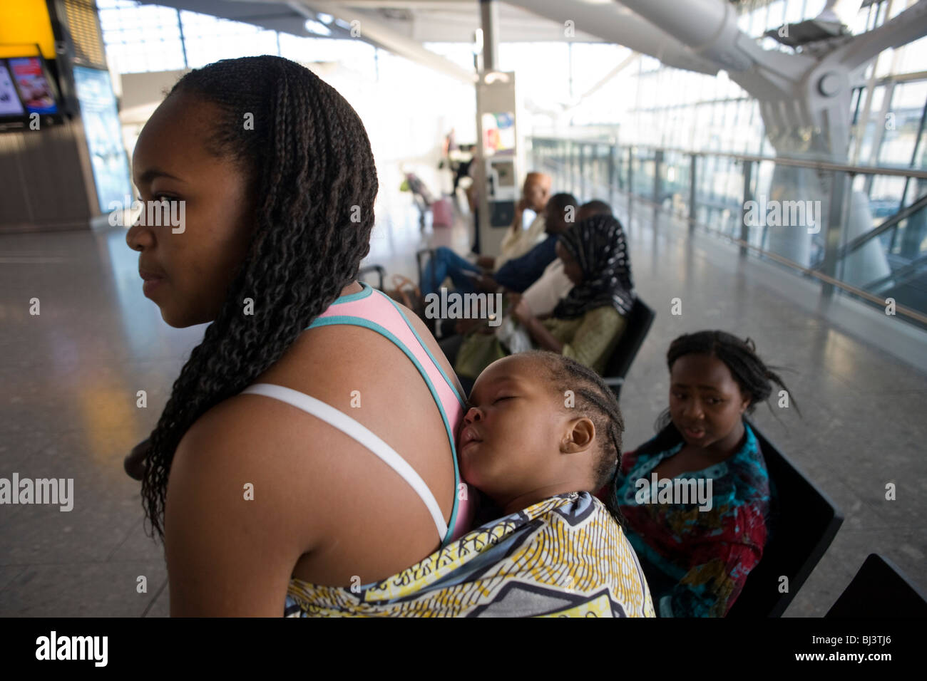 Young African mother allows her sleeping baby some well-earned rest at Heathrow Airport's Terminal 5. Stock Photo