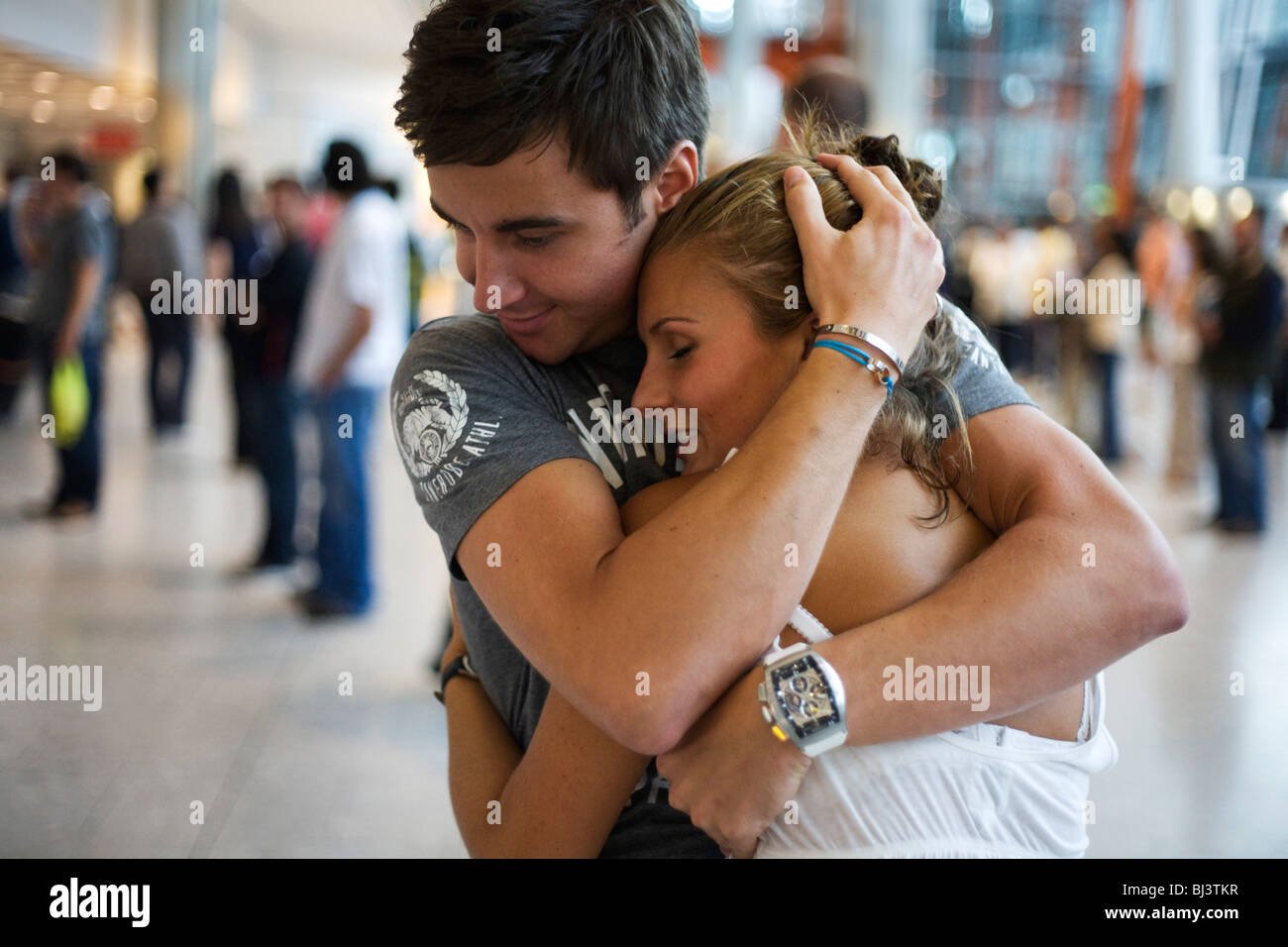 Young couple hold on to each other tight after a few weeks separation at Heathrow Airport. Stock Photo