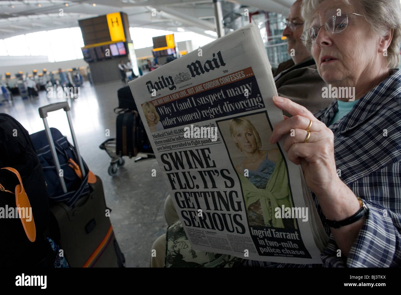 Two elderly but travel-wise passengers read the Daily Mail newspaper while awaiting their check-in zone at Heathrow airport. Stock Photo