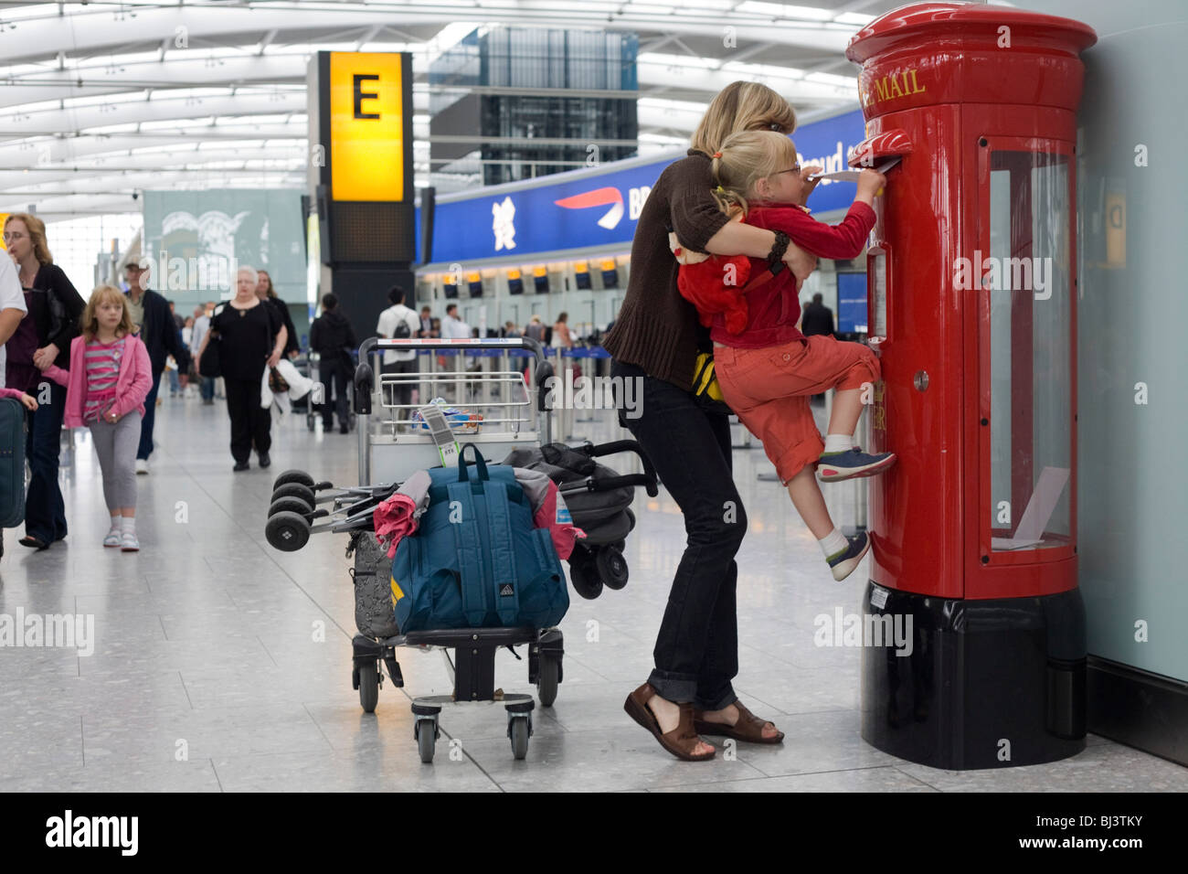 Young Mother Holds Up Her Daughter To Insert A Letter Into A Post Box 