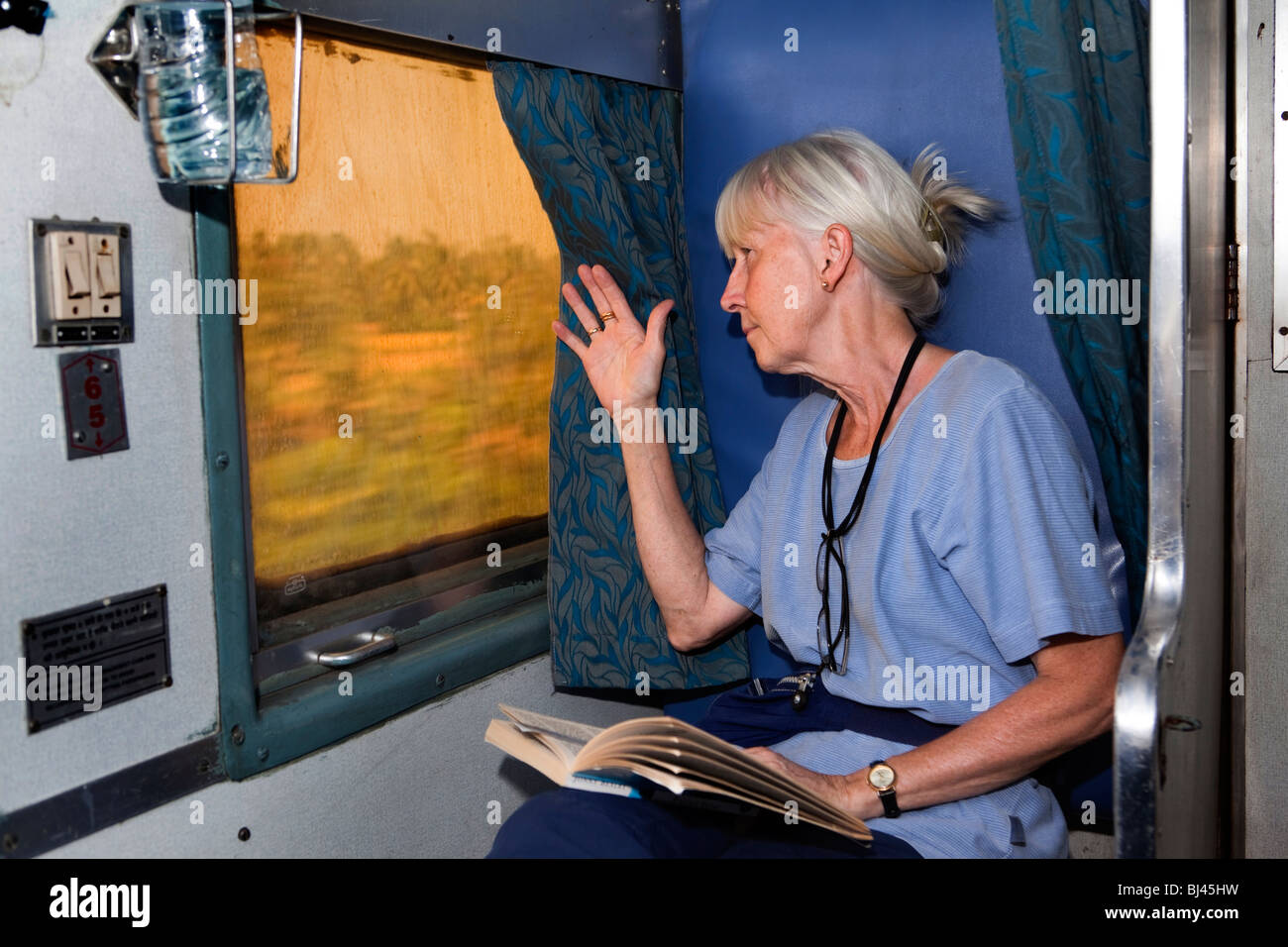 India, train travel, tourist reading book looking out of window in second class two tier air conditioned (2A) compartment Stock Photo