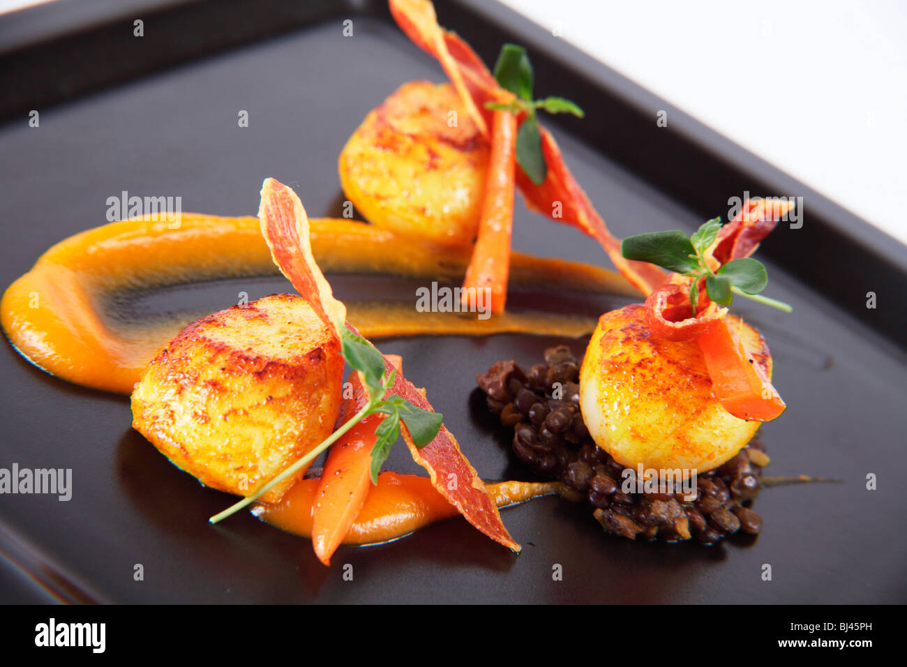 Trio of Scallops on Curried Lentils, Butternut Squash Puree and Crispy Parma Ham Stock Photo
