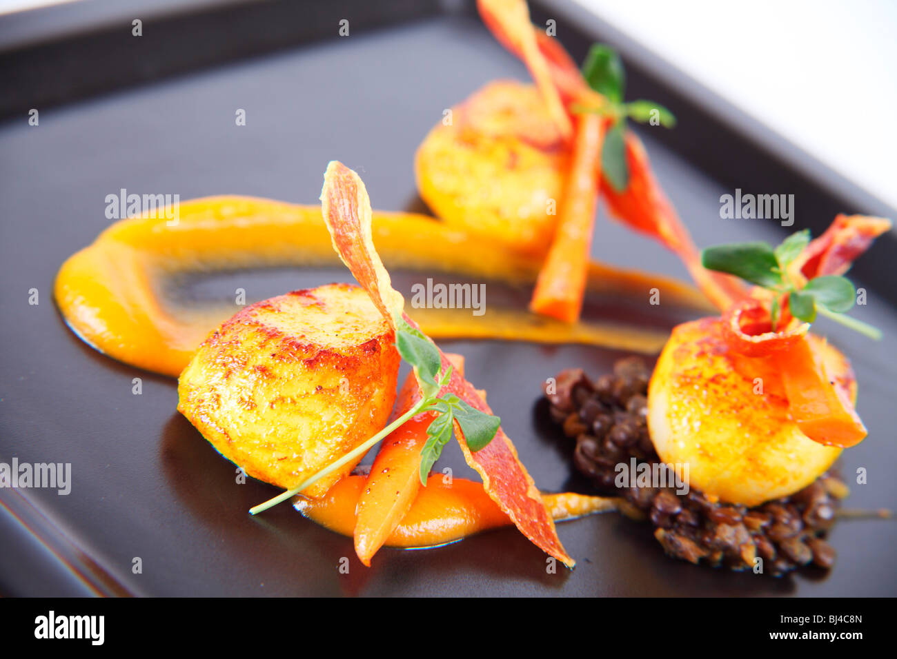 Trio of Scallops on Curried Lentils, Butternut Squash Puree and Crispy Parma Ham Stock Photo