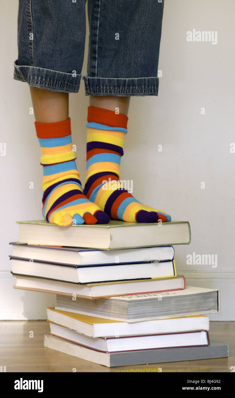 Adolescent up some books to reach an object. Stock Photo