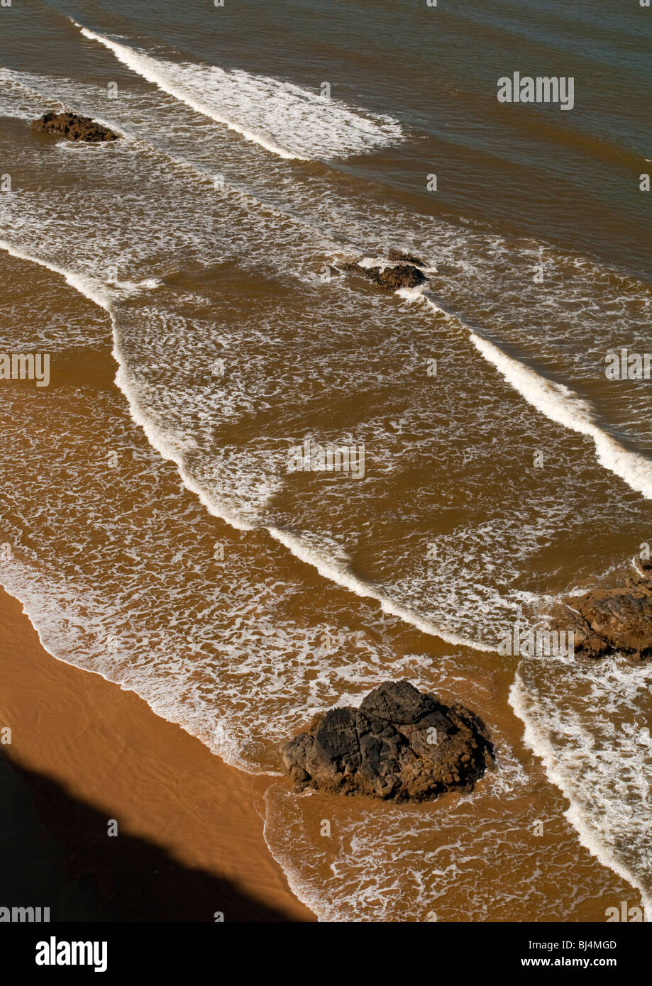 Waves crashing on a sandy beach with rocks photographed from cliffs above Stock Photo