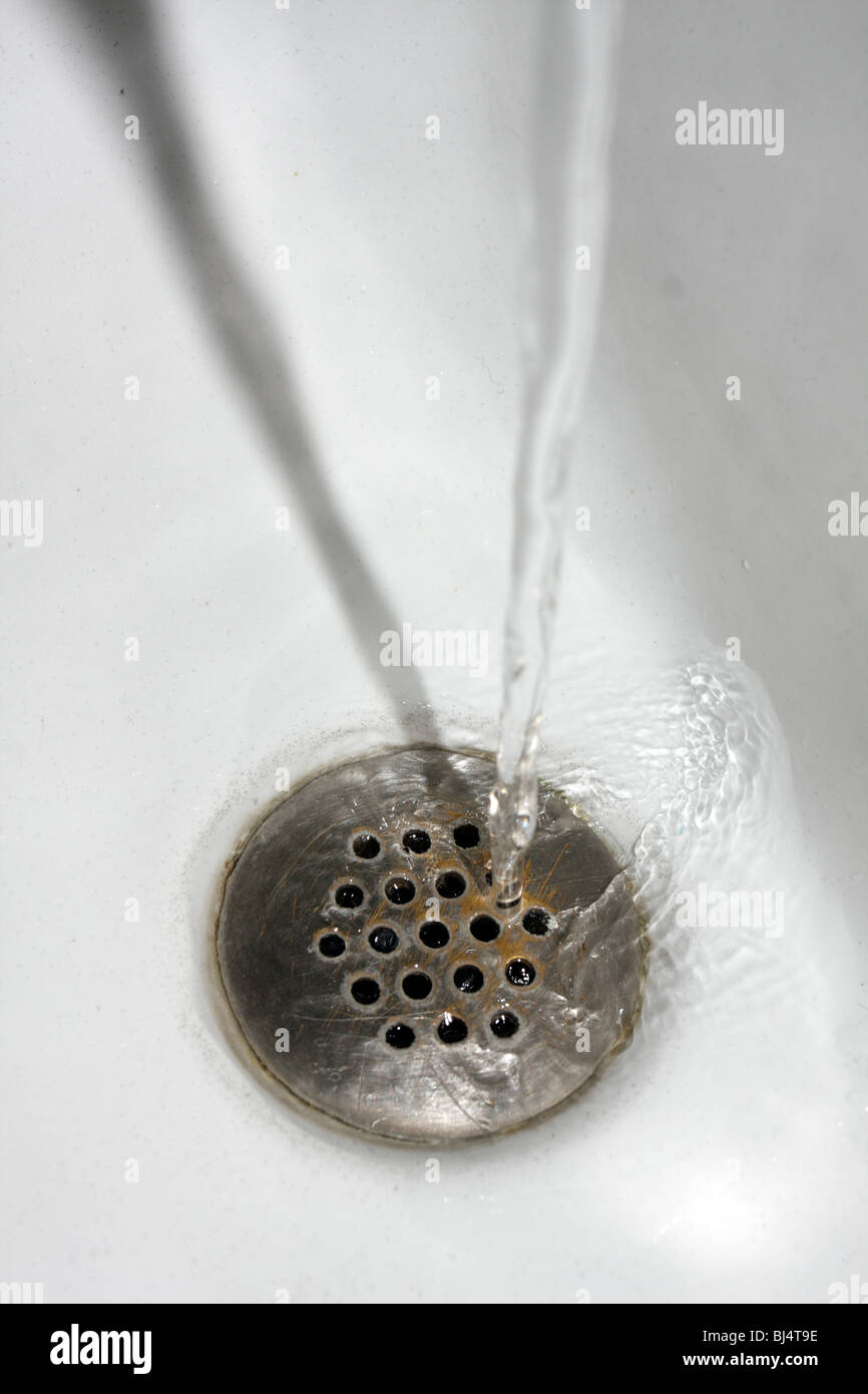 Stream of water going down a drain, landing on round grating. Stock Photo