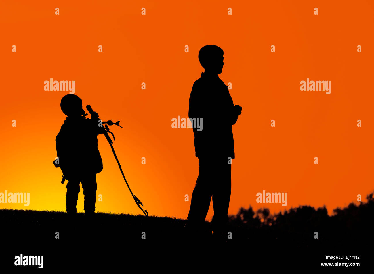 Two boys standing on a hill dark silhouette over colorful digitally adjusted orange evening sky Stock Photo