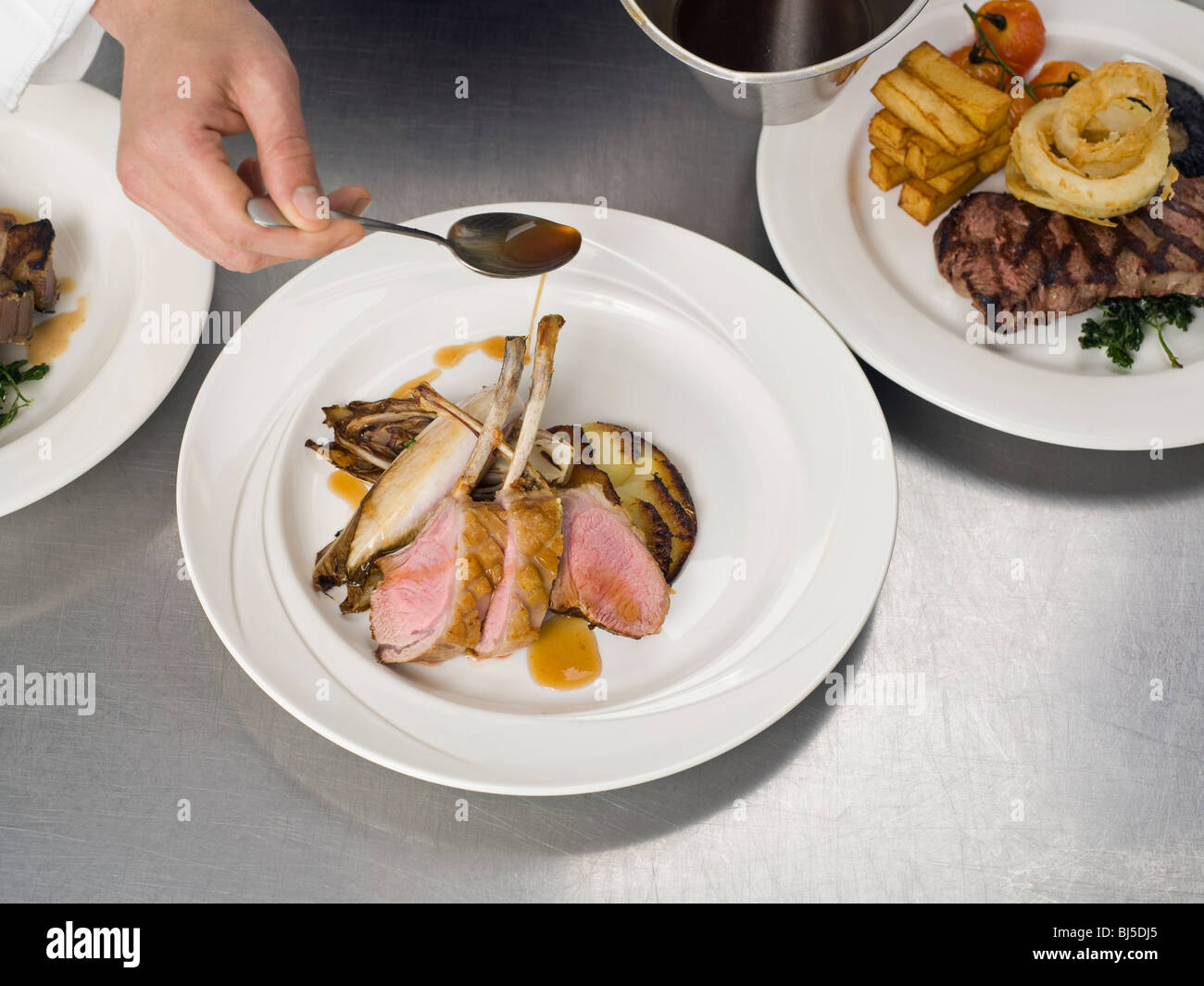 A hand drizzling gravy on some lamb Stock Photo Alamy