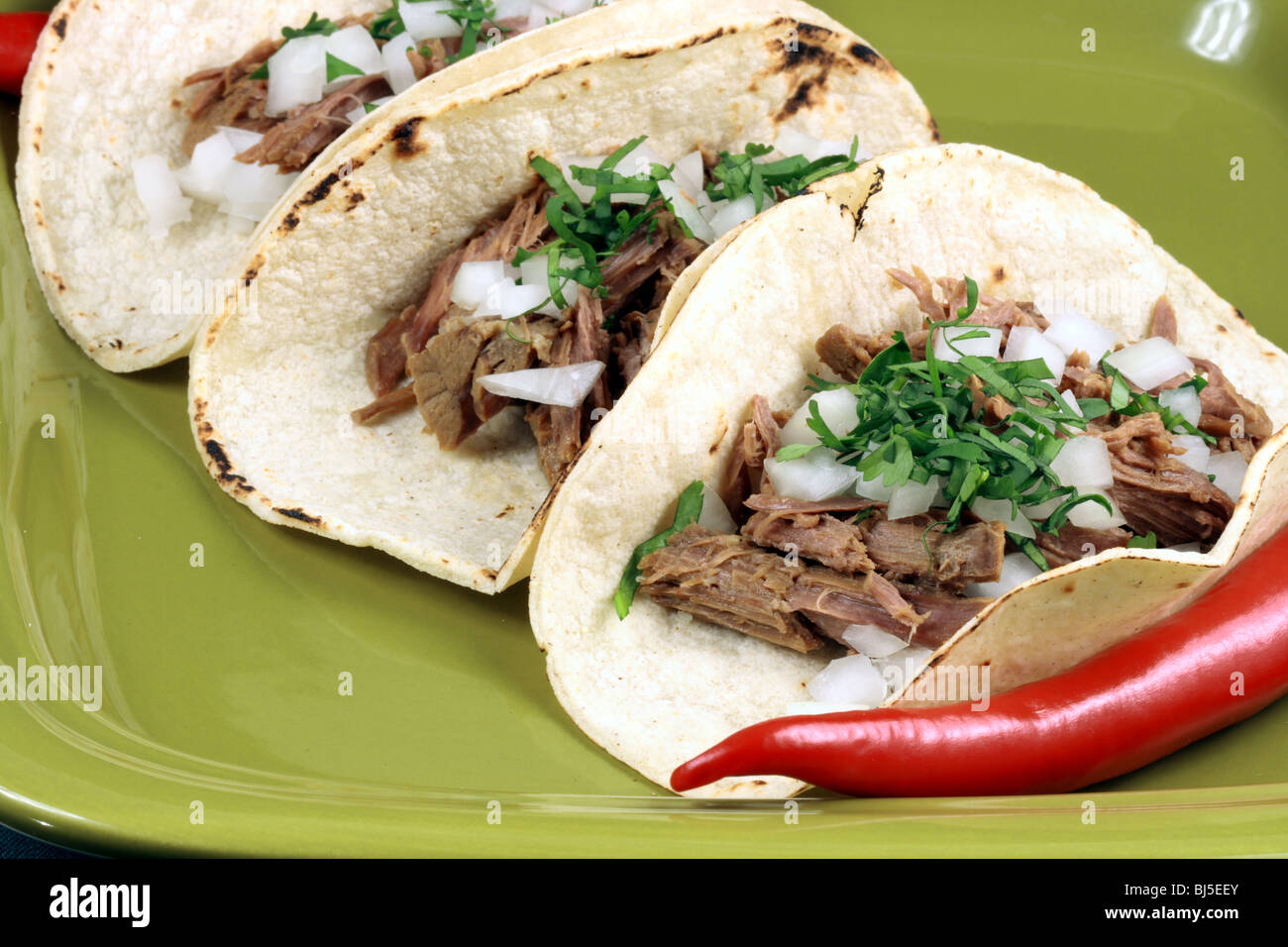 mexican tacos meal or delicious snack, made with beef, corn tortilla, cilantro and onions on a fancy green mexican style plate Stock Photo