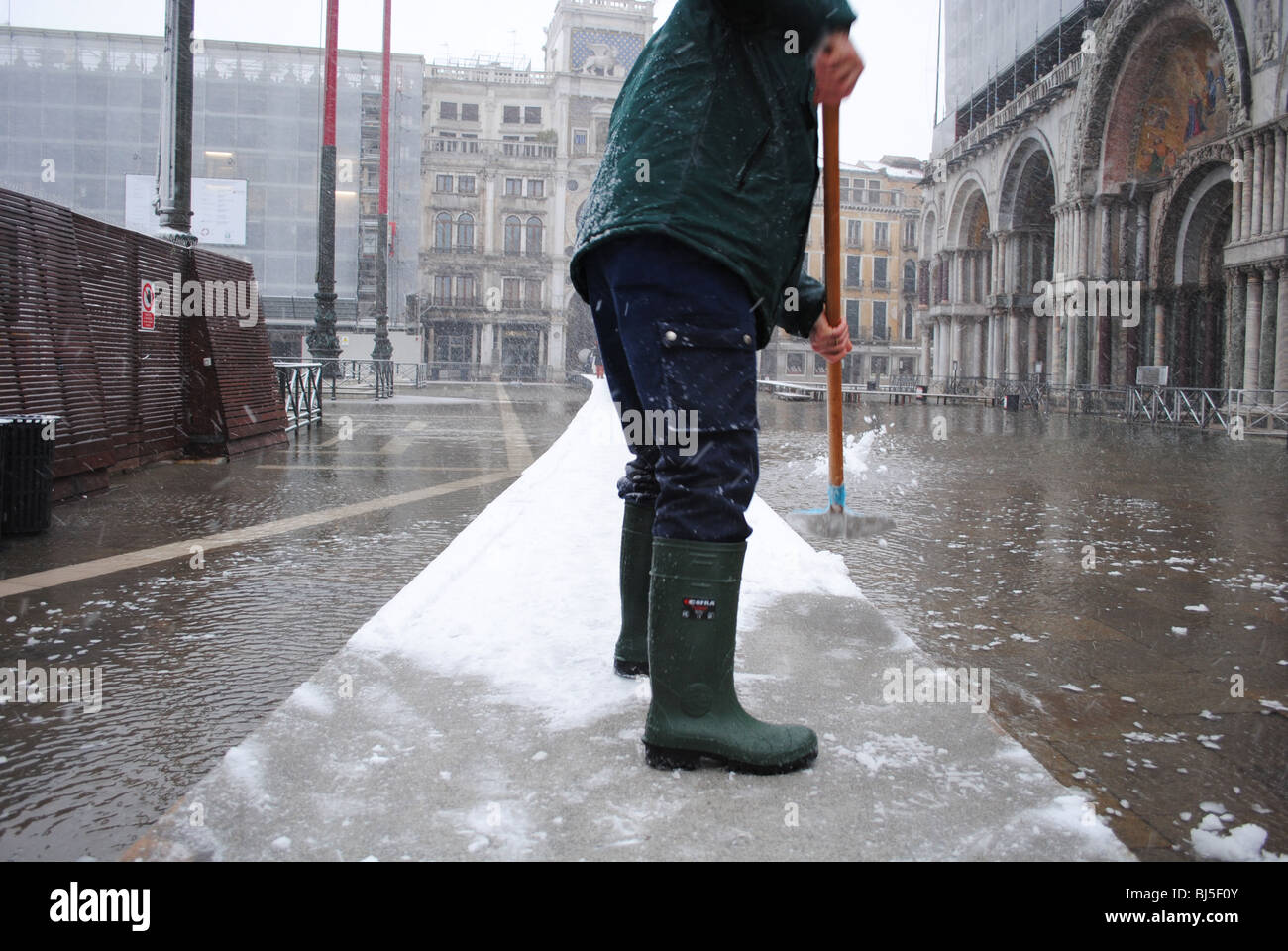 A man clears snow from walkways in a flooded St Mark's Square, Venice, Italy Stock Photo