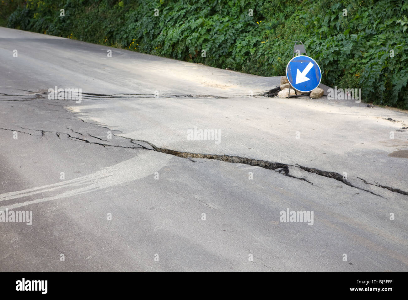 Washed out and damaged road with blue traffic sign pointing direction to attract attention Stock Photo