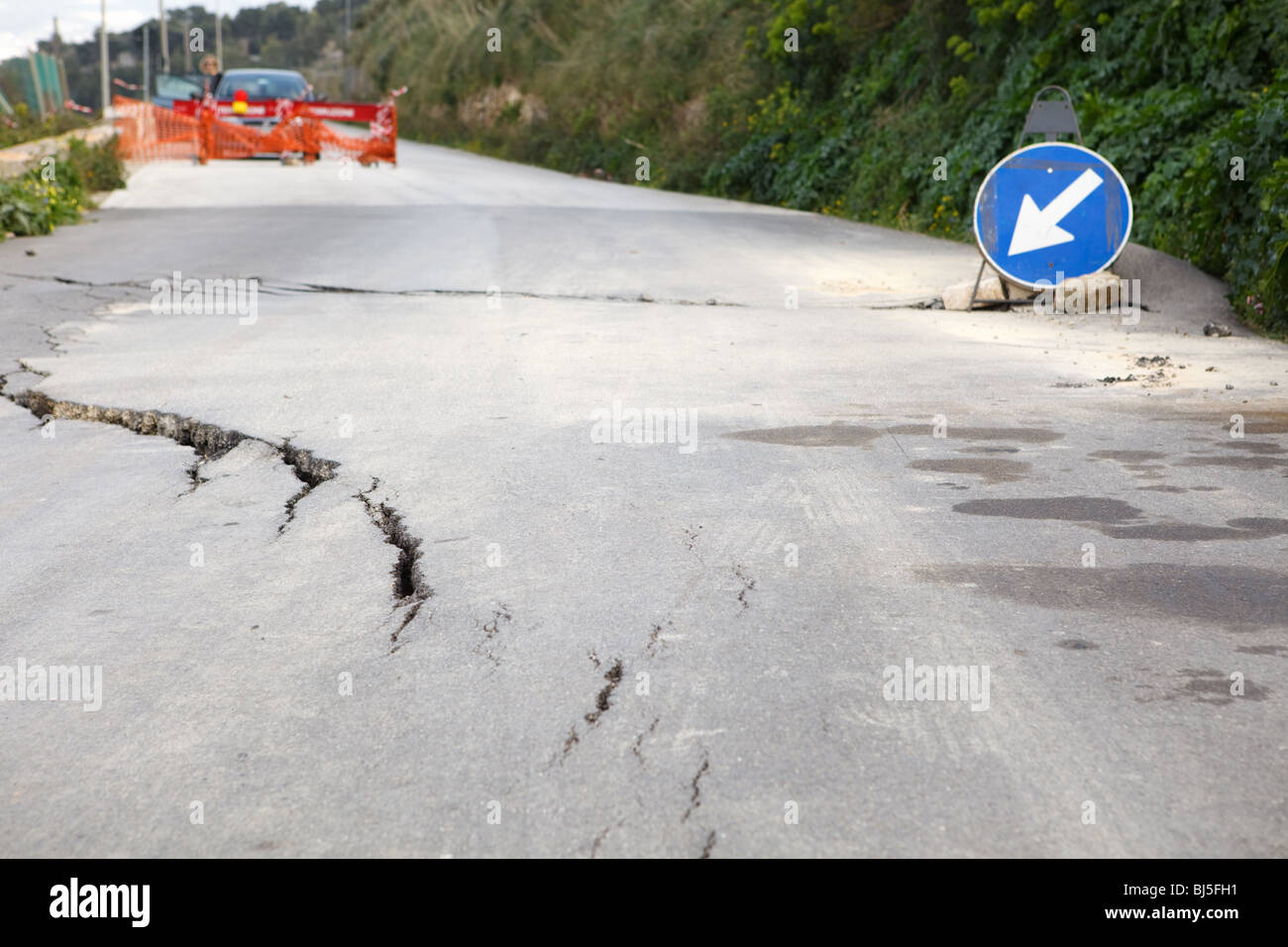 Washed out and damaged road with blue traffic sign pointing direction to attract attention Stock Photo