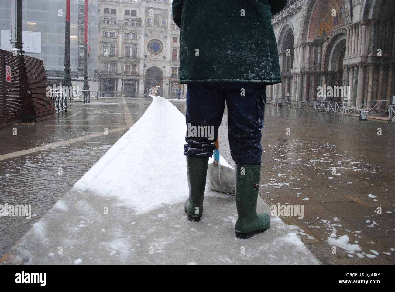 A man clears snow from walkways in a flooded St Mark's Square, Venice, Italy Stock Photo