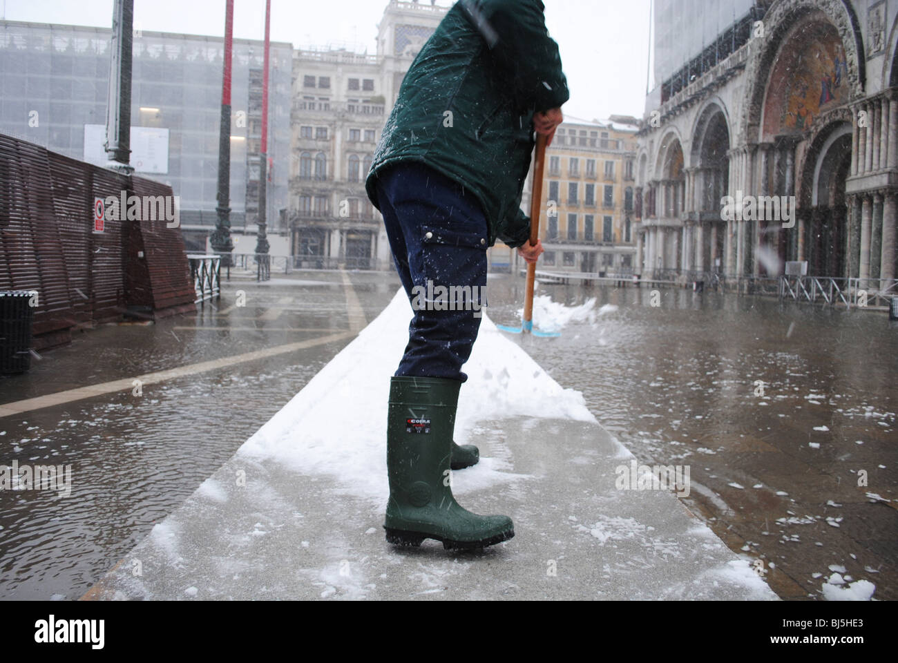 A man clears snow from walkways in a flooded St Mark's Square, Venice, Italy Stock Photo
