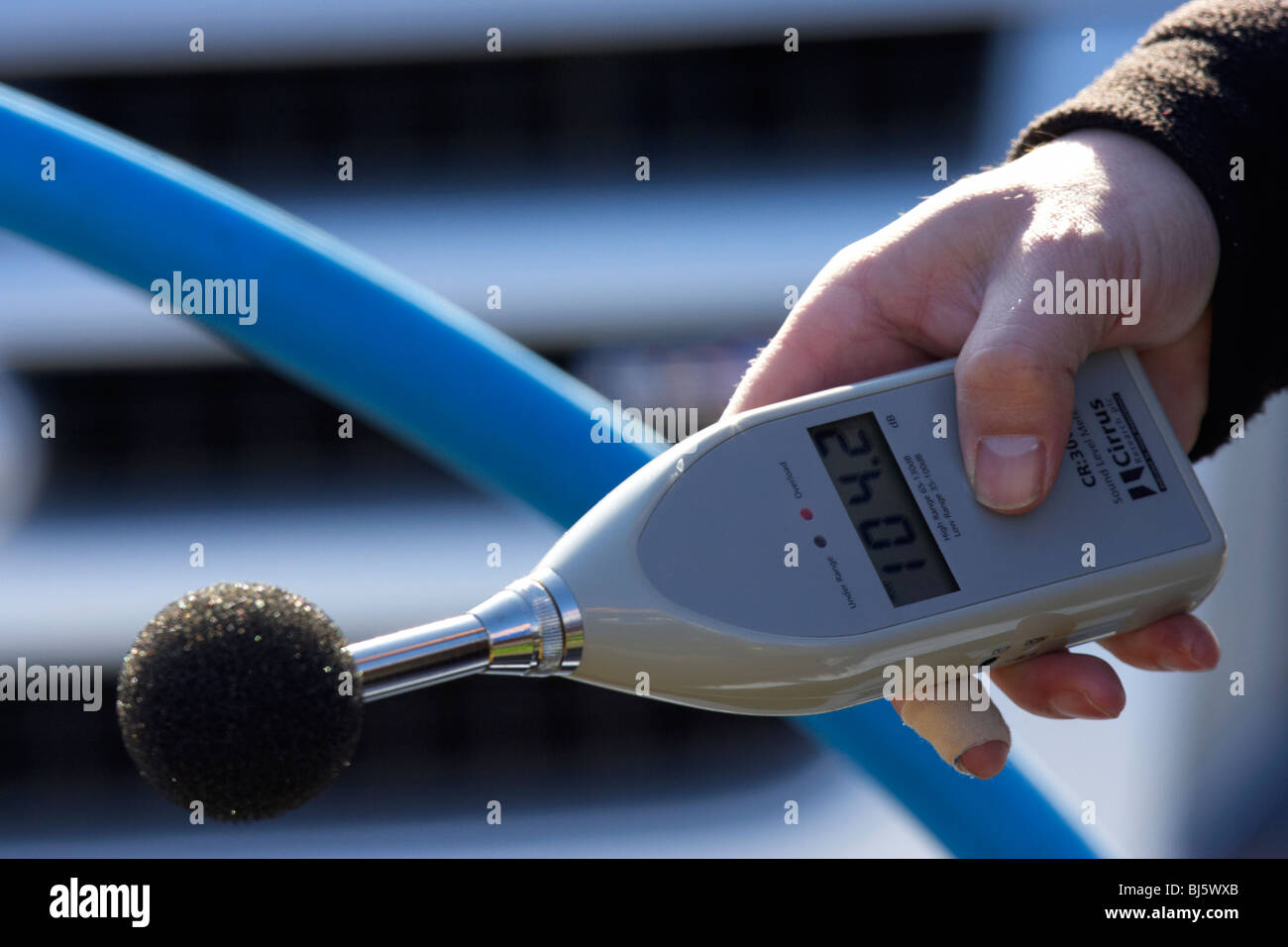 mans hand holding sound level meter with baffle showing measurement of 104.2 dB the meter is used to measure maximum noise Stock Photo