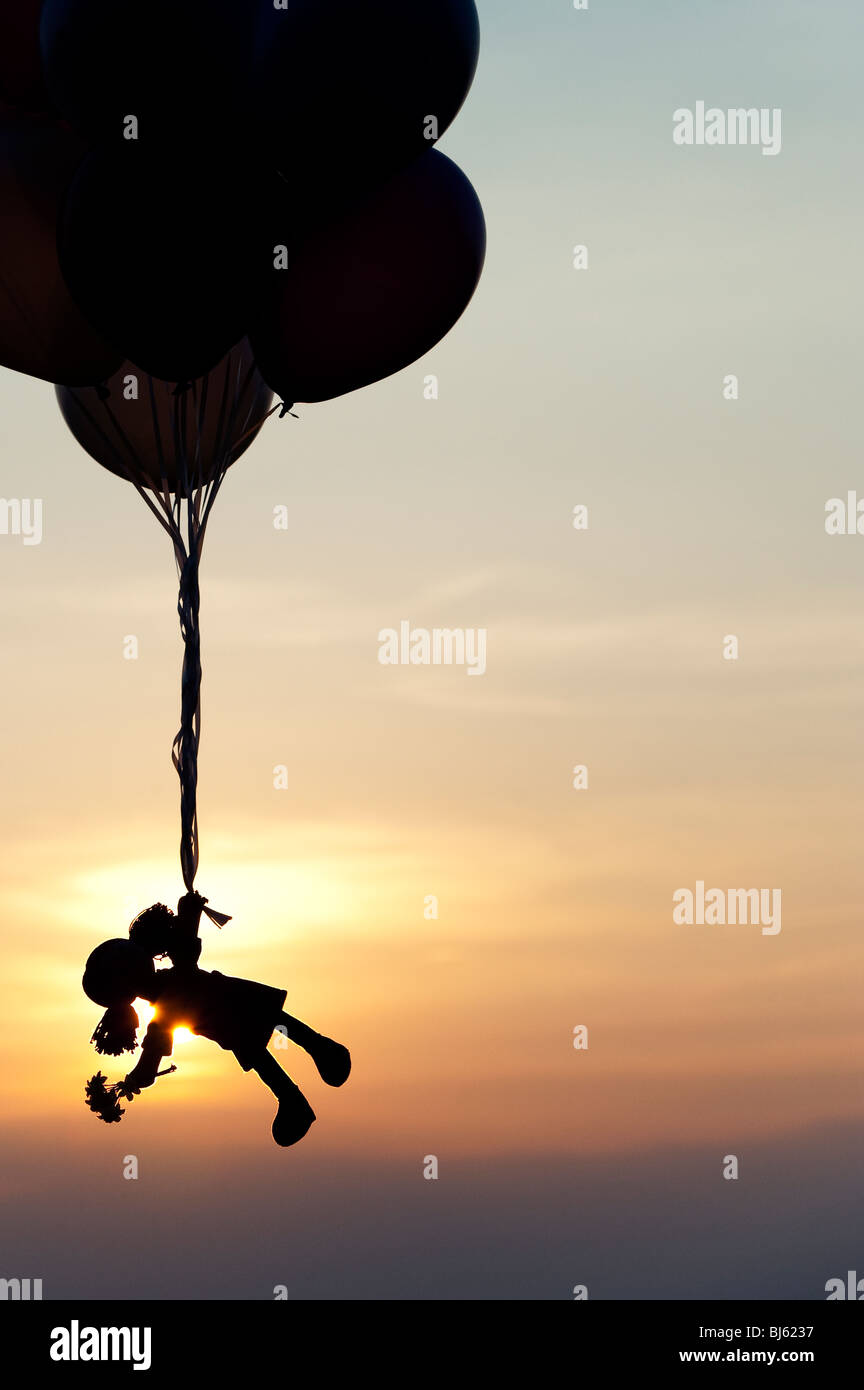 Rag doll holding onto helium balloons floating away at sunset. Silhouette Stock Photo