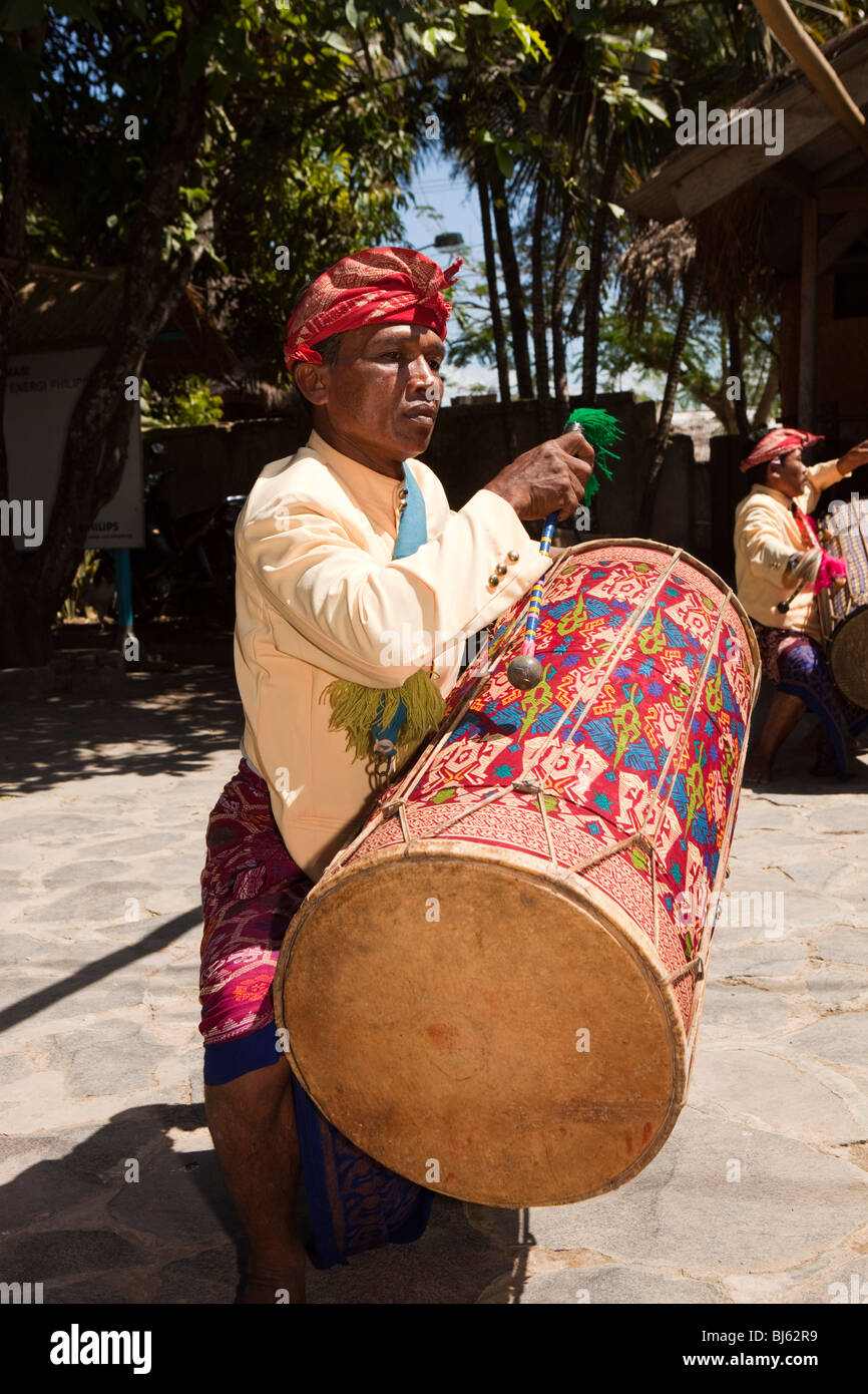 Indonesia, Lombok, Sade, traditional Sasak village, man drumming to welcome visiting party of tourists Stock Photo
