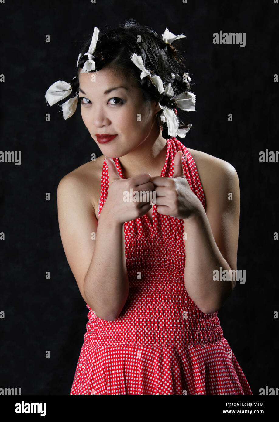 Happy Smiling Chinese Girl Wearing a White Spotted Red Dress with Paper Ties in Her Hair. Stock Photo