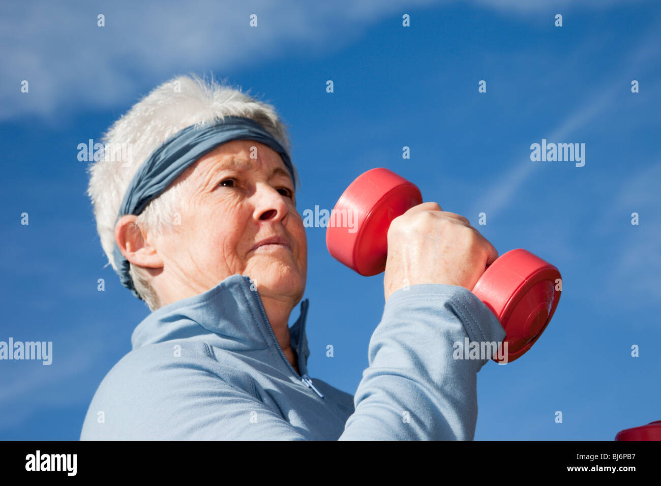 Elderly senior woman OAP lady wearing a sweatband whilst exercising with dumbbell hand weights outdoors. Britain, UK. Stock Photo