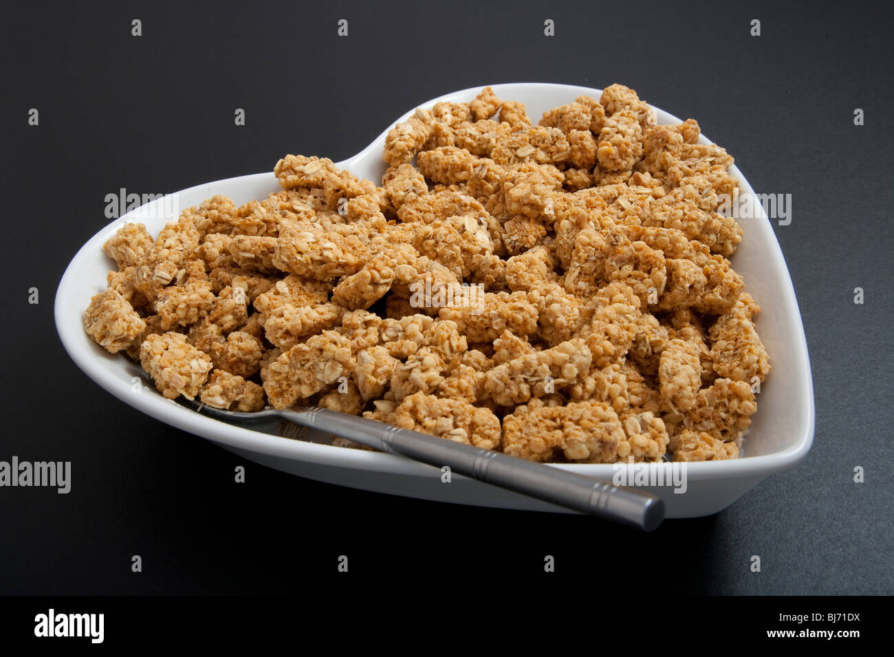 Heartshaped cereal bowl or dish, with spoon and cereals on black