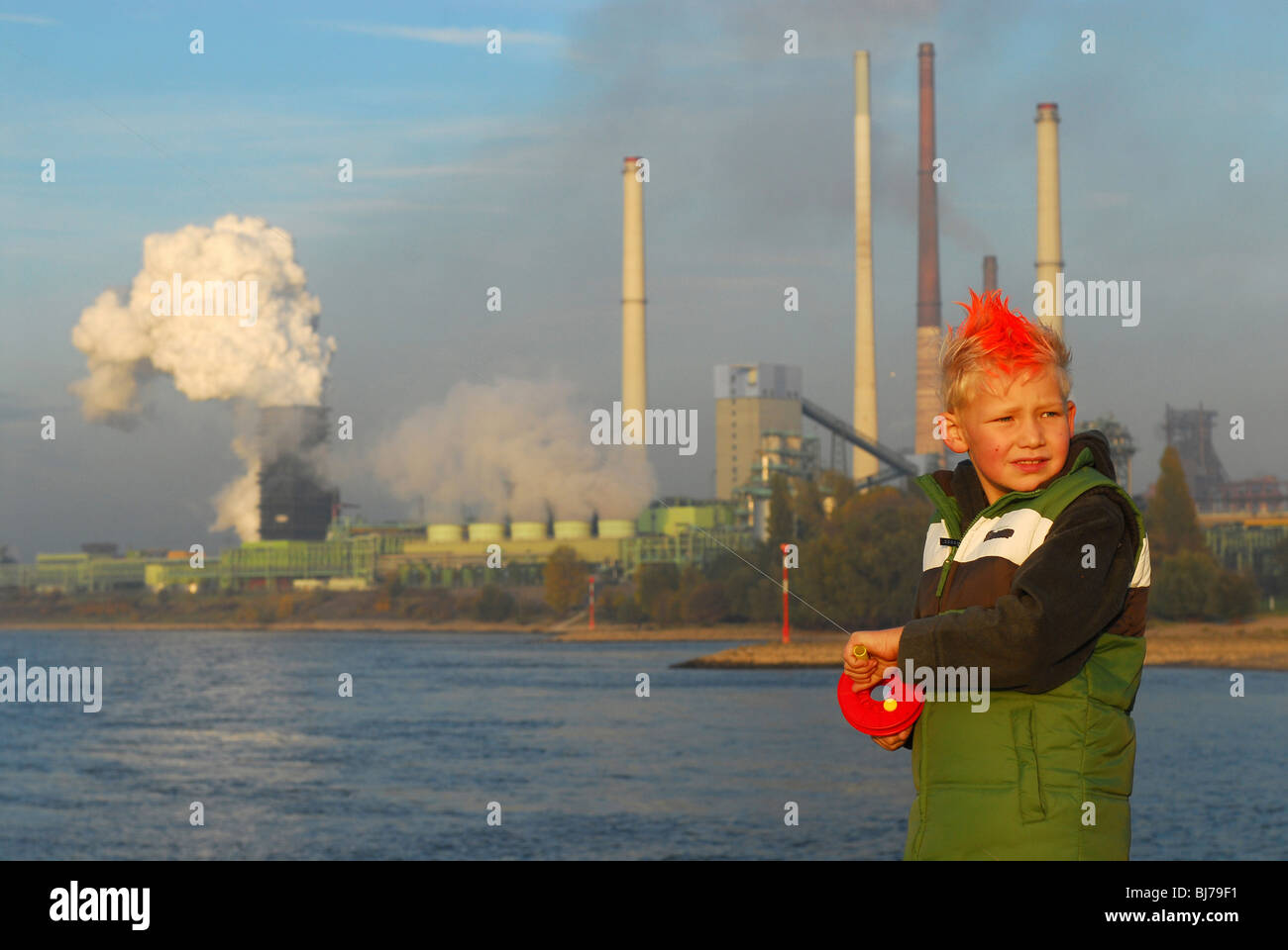 Boy standing by a river with the ThyssenKrupp Stahl AG coking plant in the background, Duisburg, Germany Stock Photo