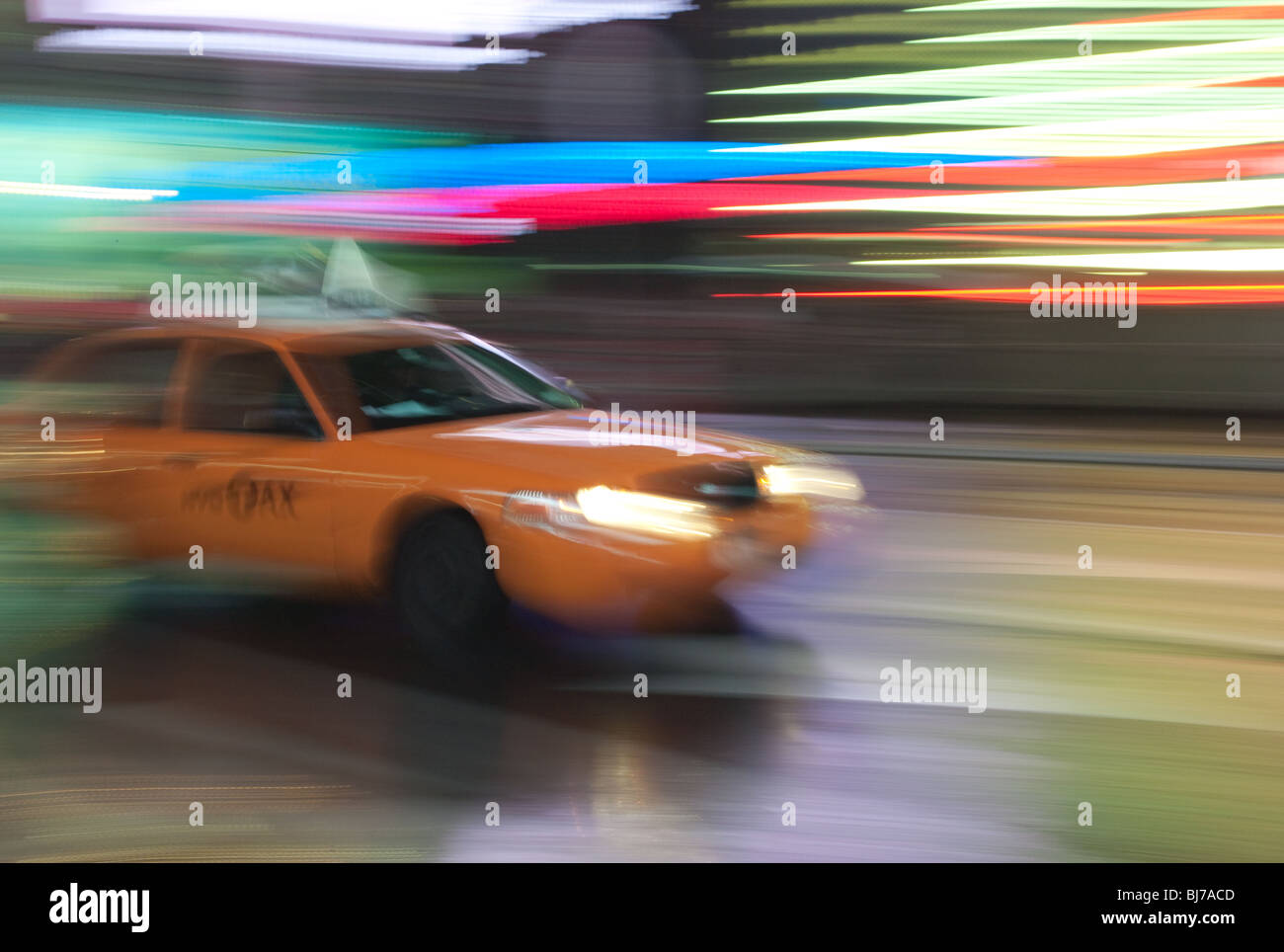A yellow taxi cab is a blur as it rushes through the lights of Times Square at night in New York City. Stock Photo
